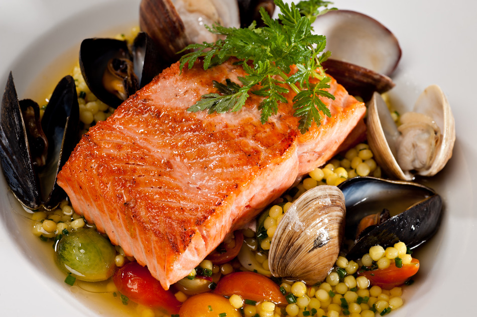 Beautifully plated salmon fillet garnished with colorful green parsley. Served over a couscous and seafood salad featuring mussels, clams, tomatoes and brussels sprouts.