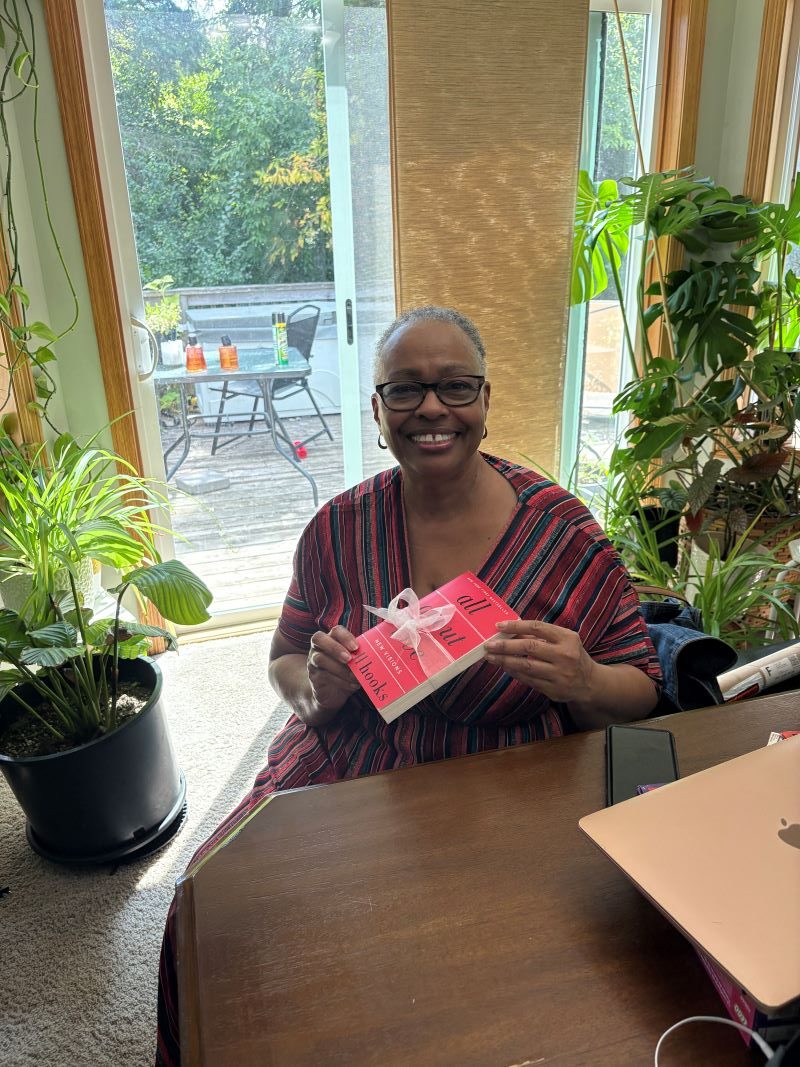 My mother sitting at the kitchen table in a red dress, smiling as she holds the book by her favorite author that she received as a birthday gift.