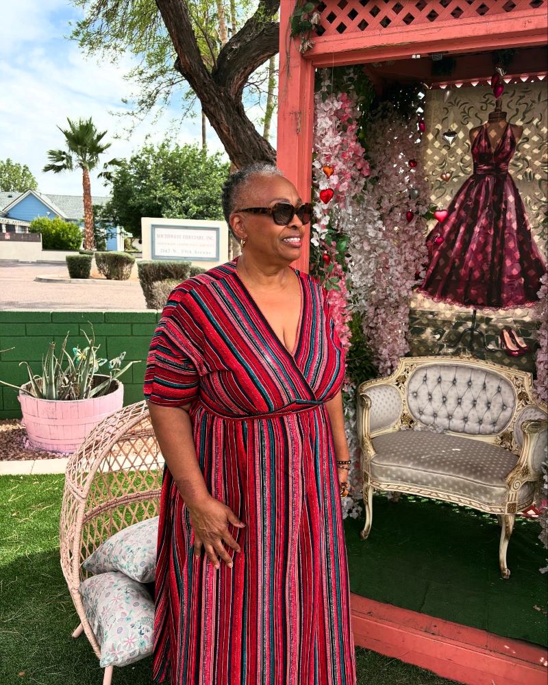 Woman posing in front of a decorative outdoor vignette at The Pink Door Tea House, featuring a vintage table-and-chair setup.