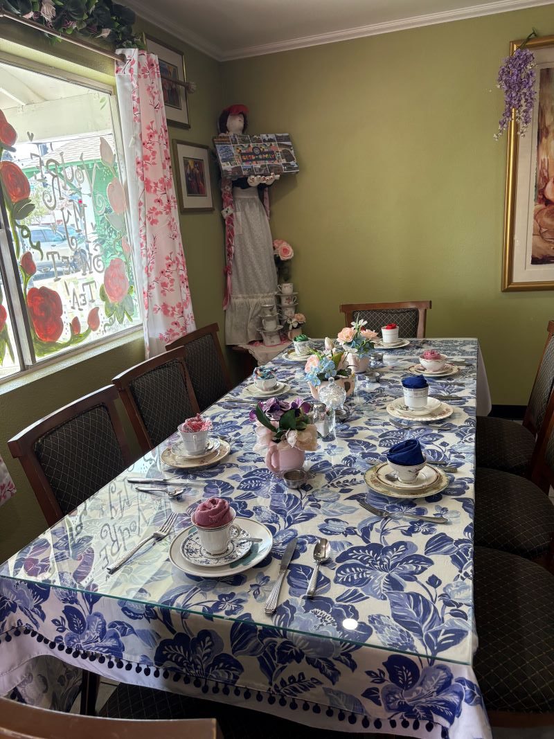Tables inside The Pink Door Tea House set with floral tablecloths, vintage tea sets, and assorted utensils.